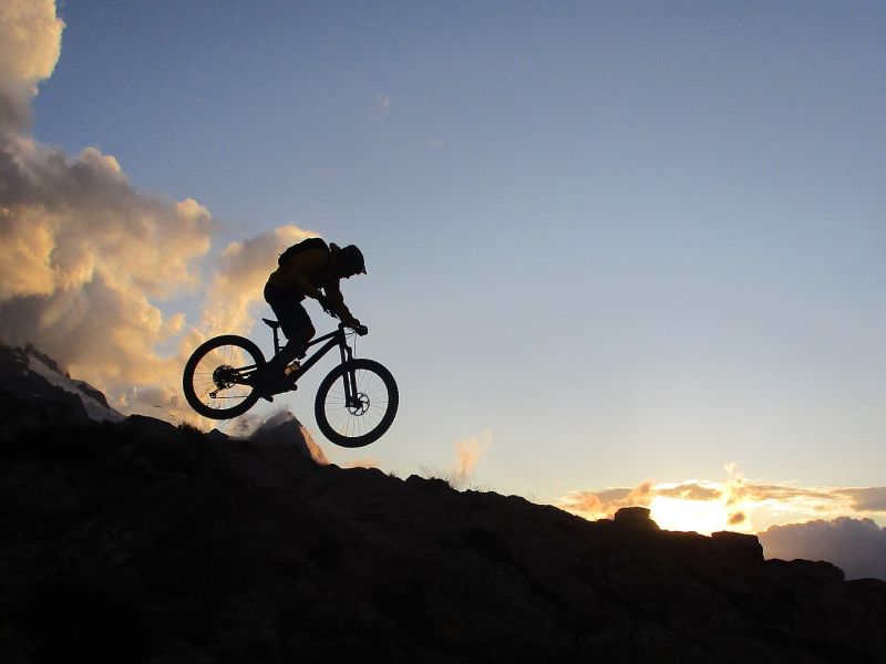 Mountainbiker im Gegenlicht vor der Meije bei Sonnenuntergang